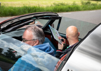 Twee mannen in een auto met open dak. Ze orienteren op een rallyroute en beslissen welke weg ze willen rijden.